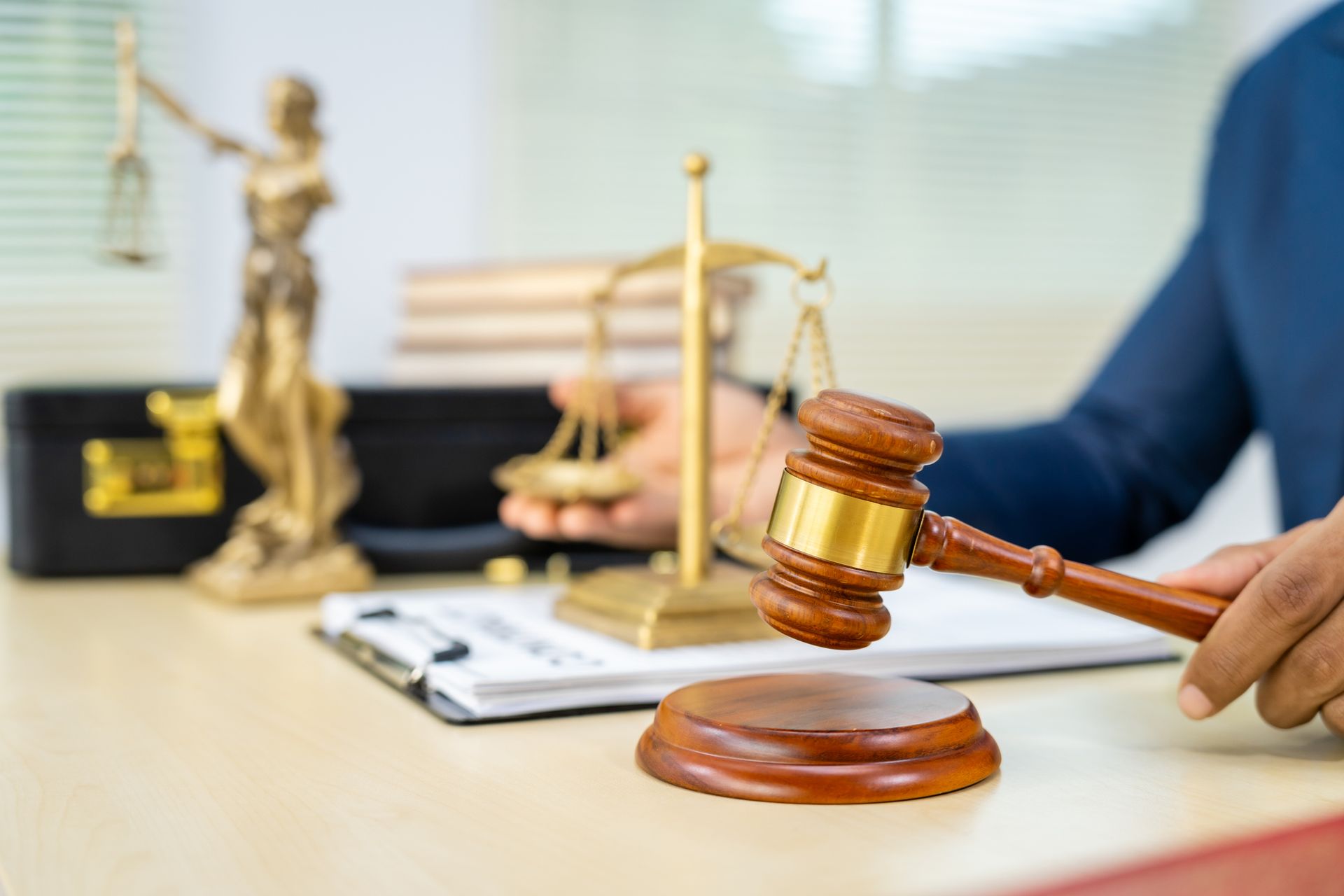A judge is holding a wooden gavel in front of a statue of justice.