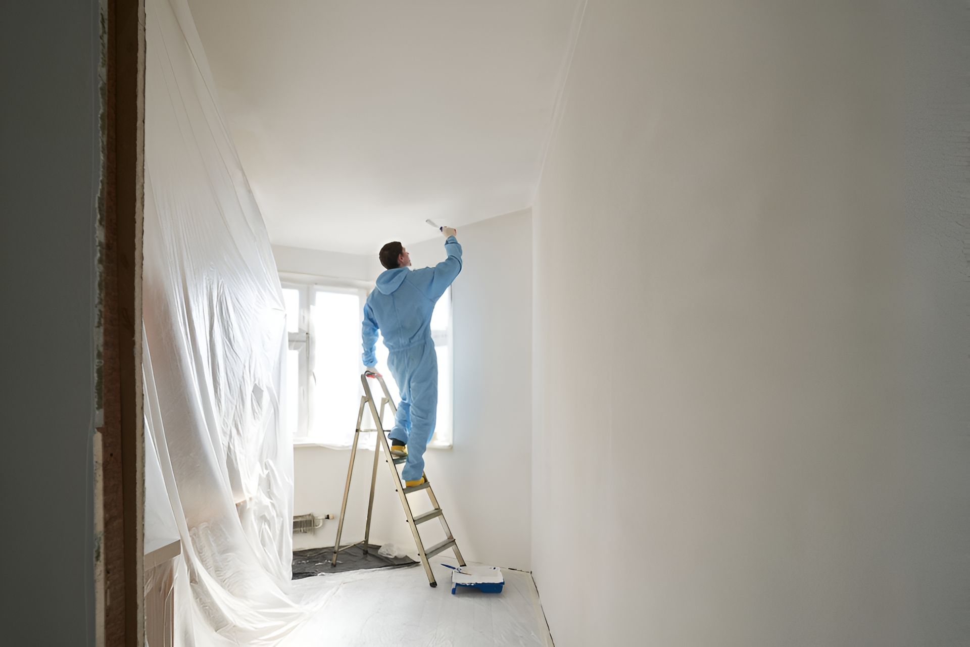 A Man is Painting a Wall With a Paint Roller — A-Z Property Painting In Karuah, NSW