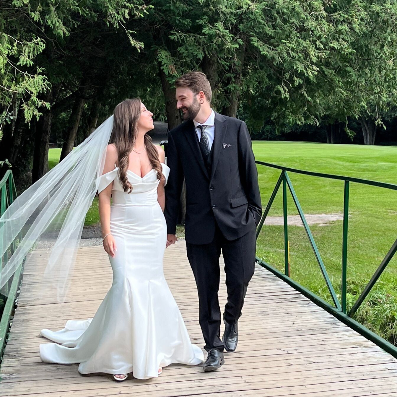 A bride and groom are walking across a bridge.