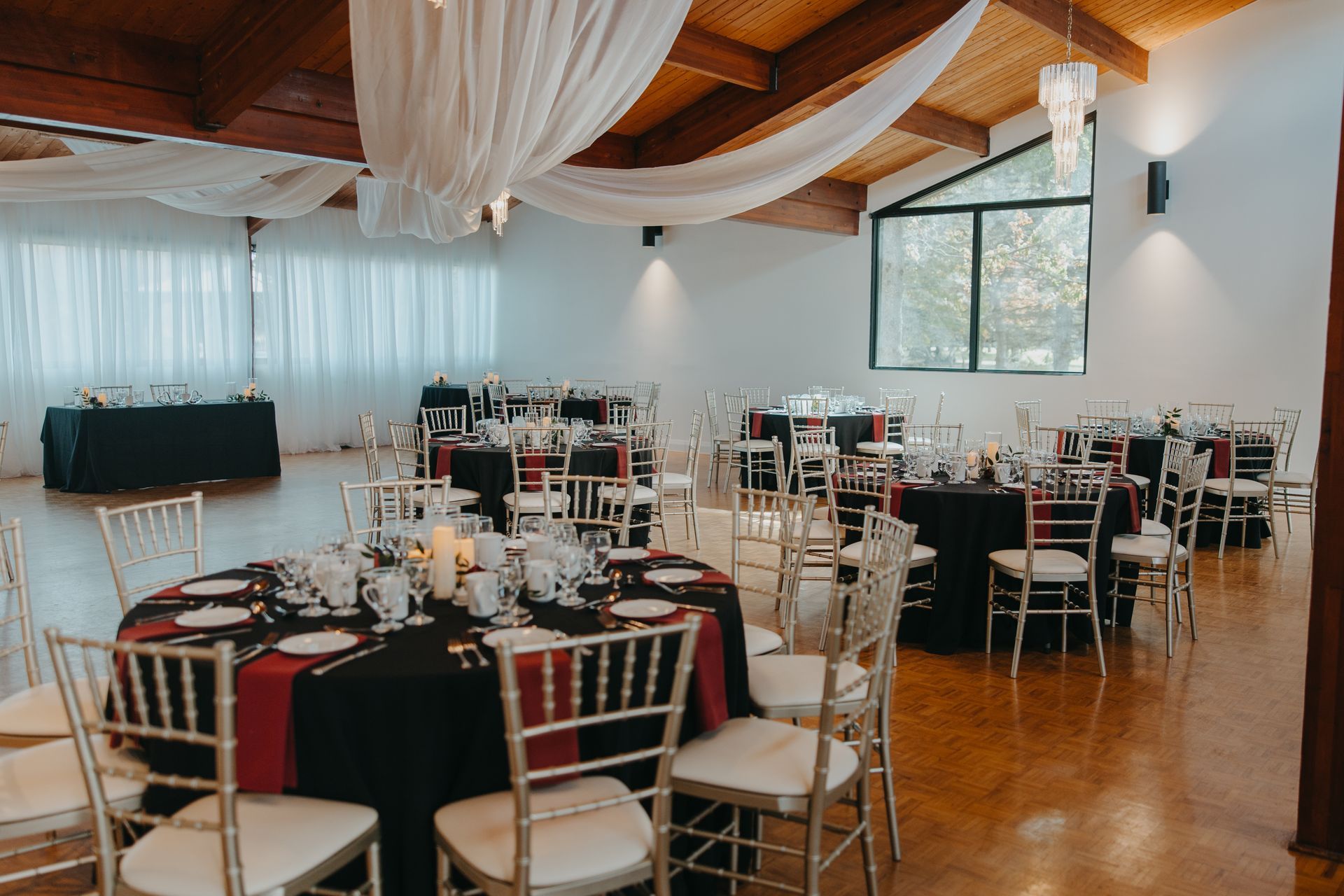 A large room with tables and chairs set up for a wedding reception with white drapery on the ceiling.