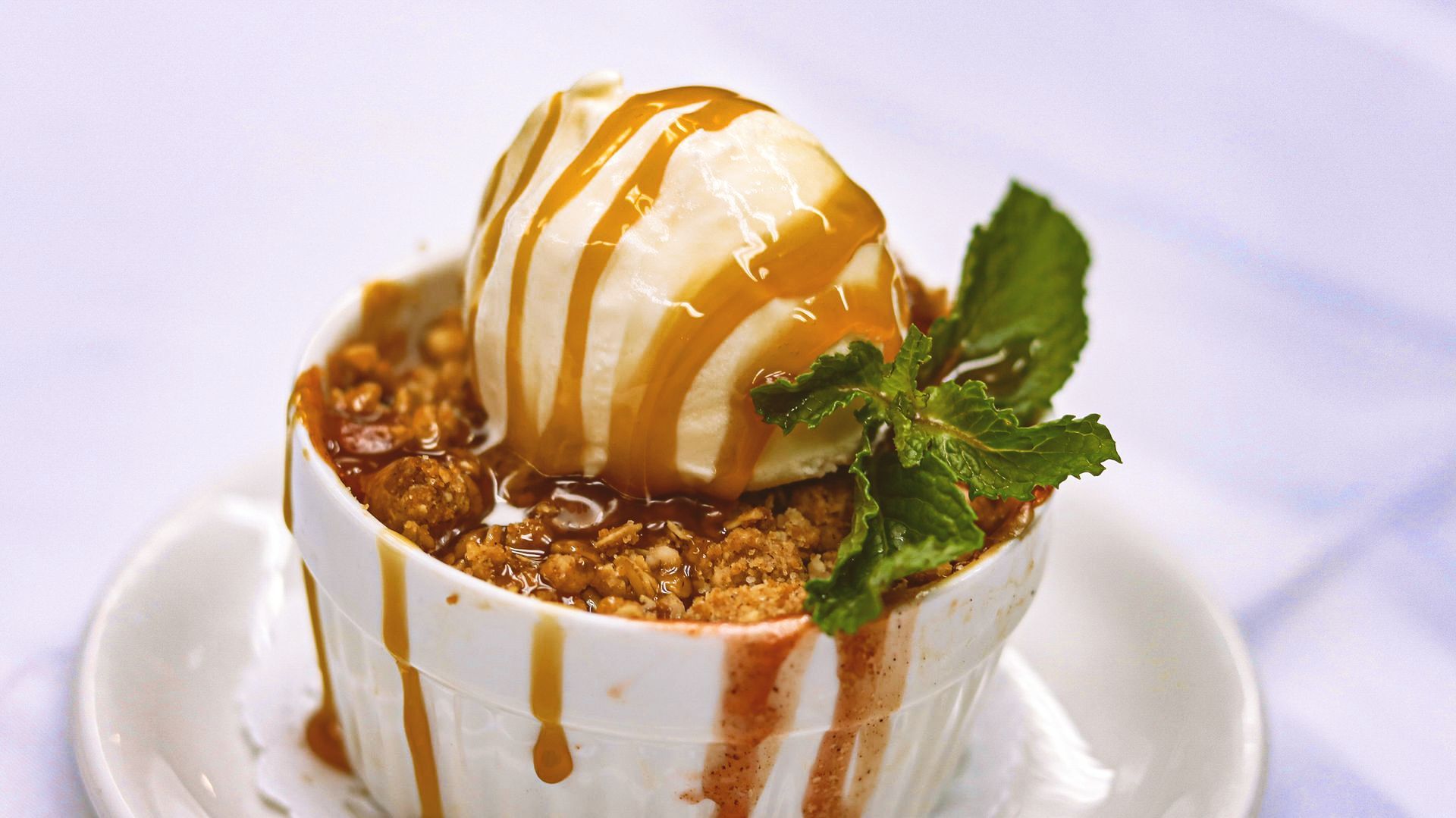 A close up of apple crumble with ice cream and caramel sauce and mint.