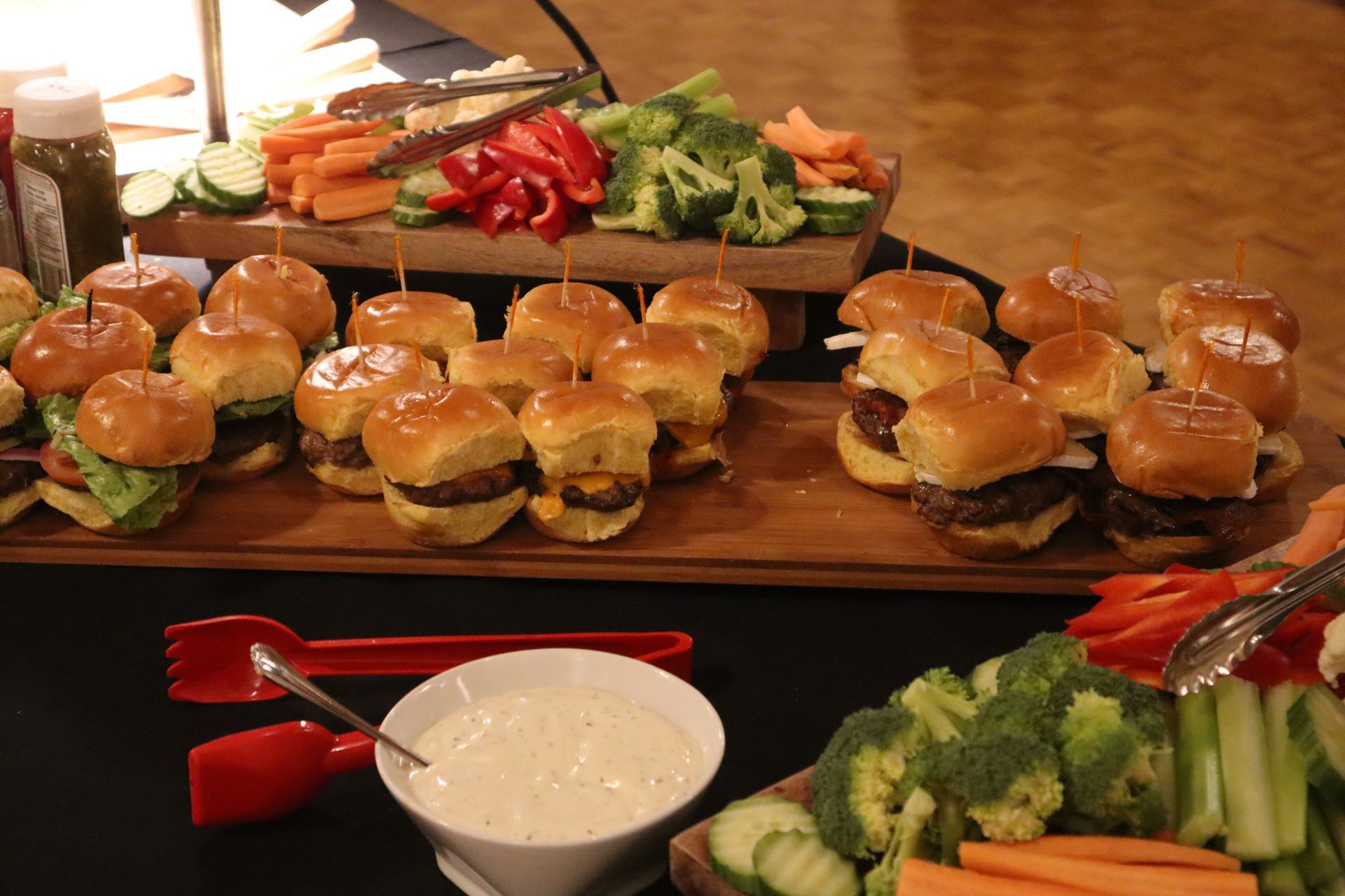 A buffet table with sliders and vegetables on wooden boards.