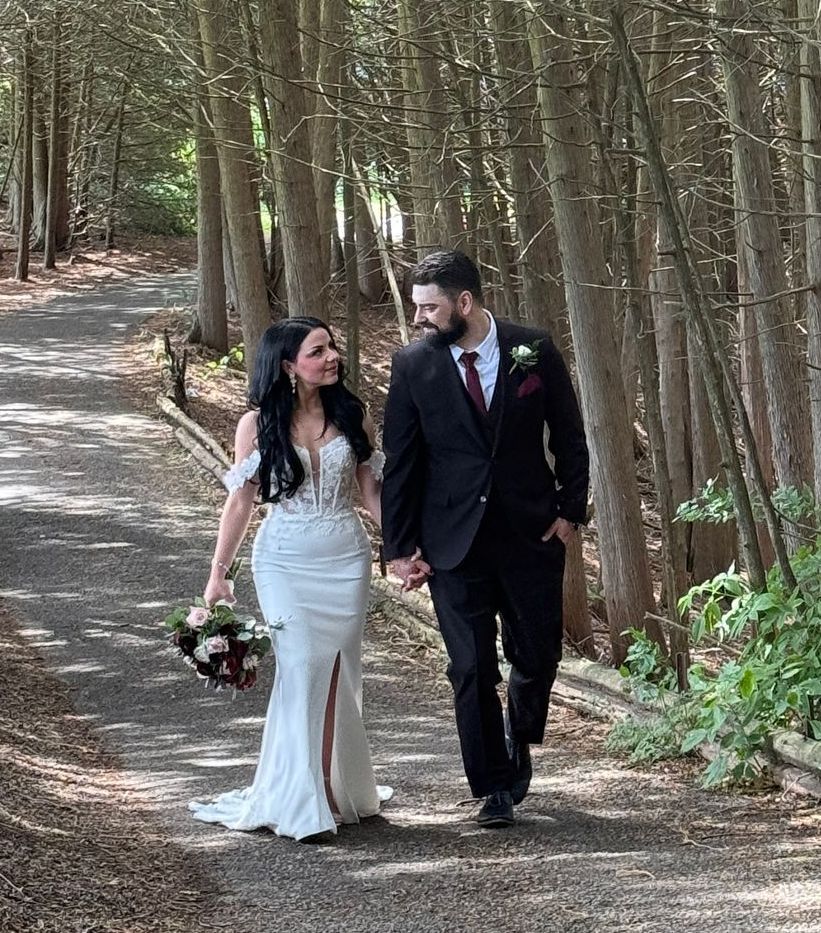 A bride and groom are walking down a path in the woods.