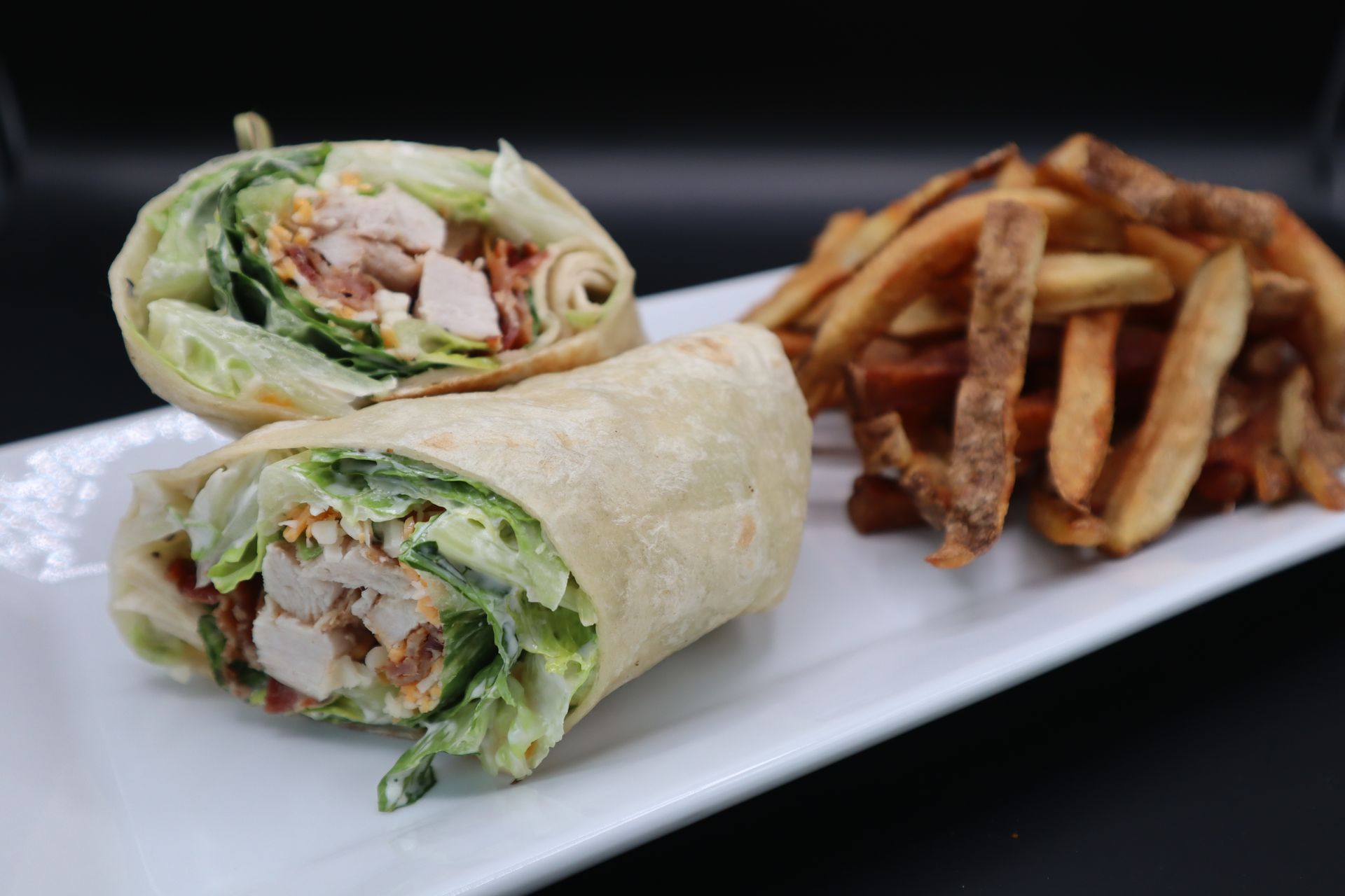 A chicken caesar wrap and french fries on a white plate.