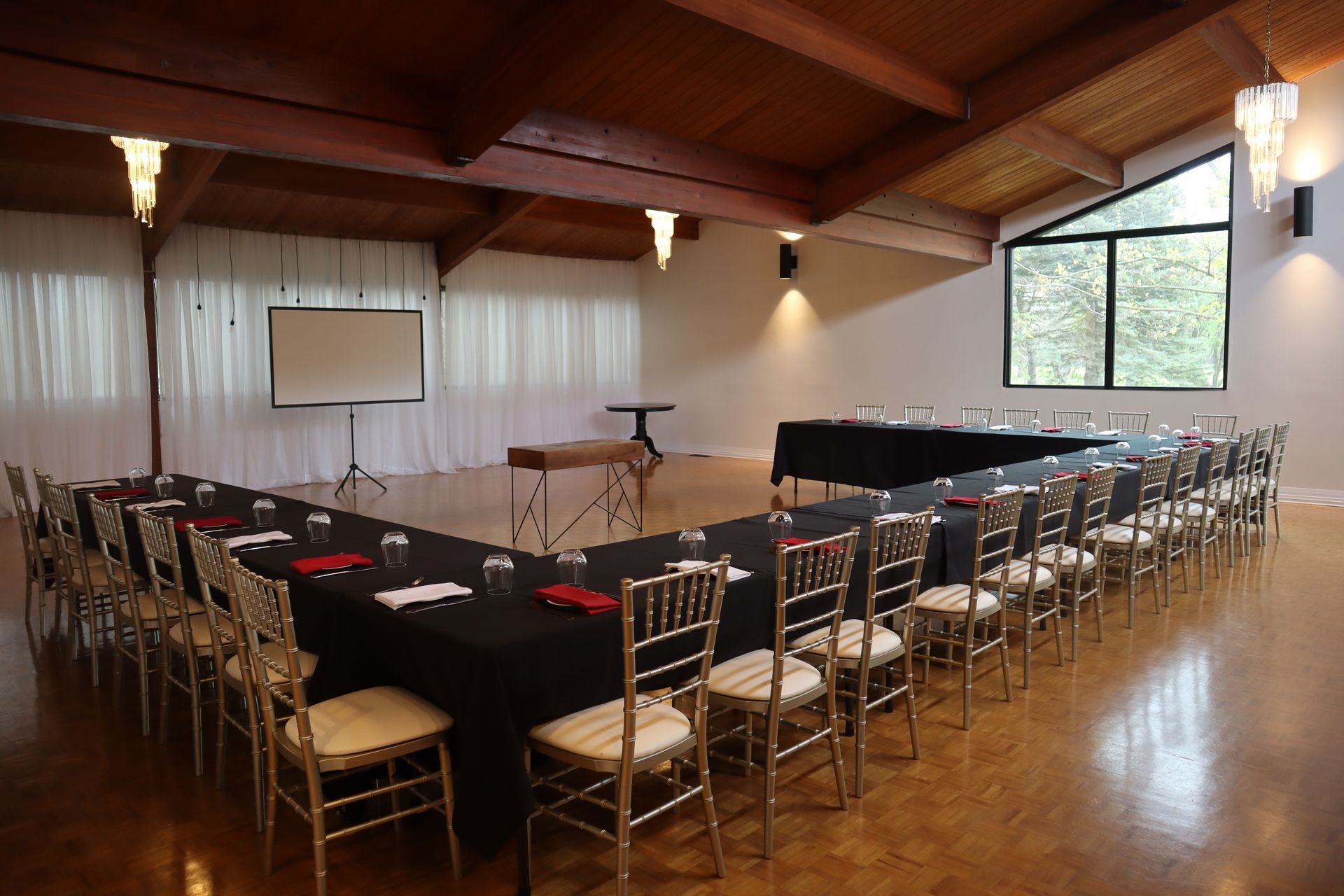 A large room with tables and chairs and a projector screen.