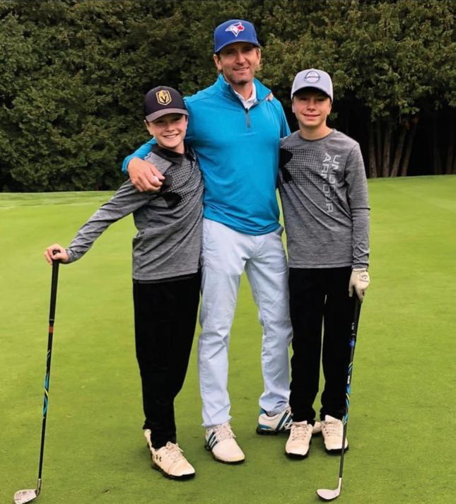 A man, Mark Gibson, and his two sons pose for a picture on a golf course