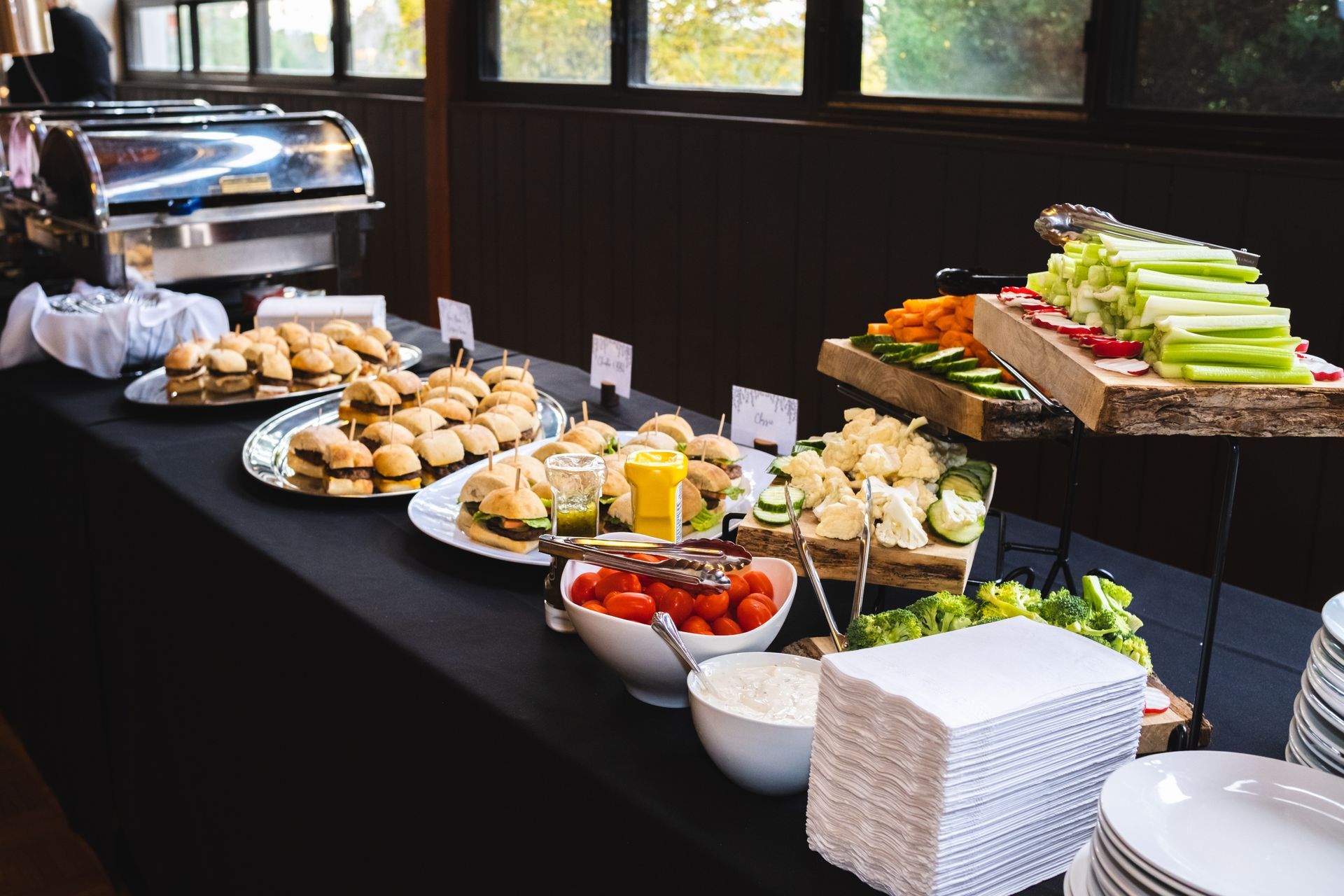 Buffet table with tiered charcuterie wood boards with vegetables on them, and sliders.