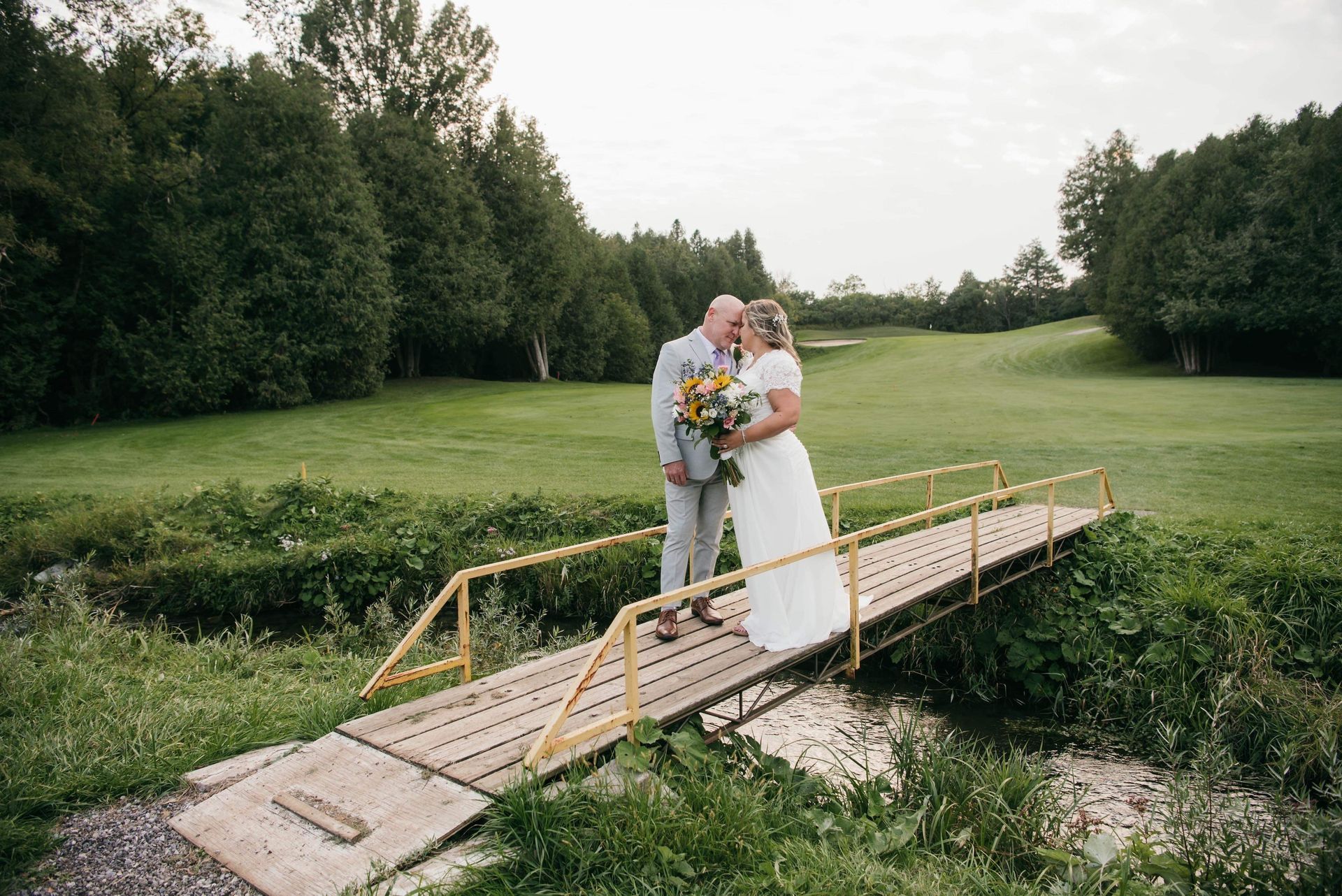 A bride and groom are kissing on a wooden bridge over a river.