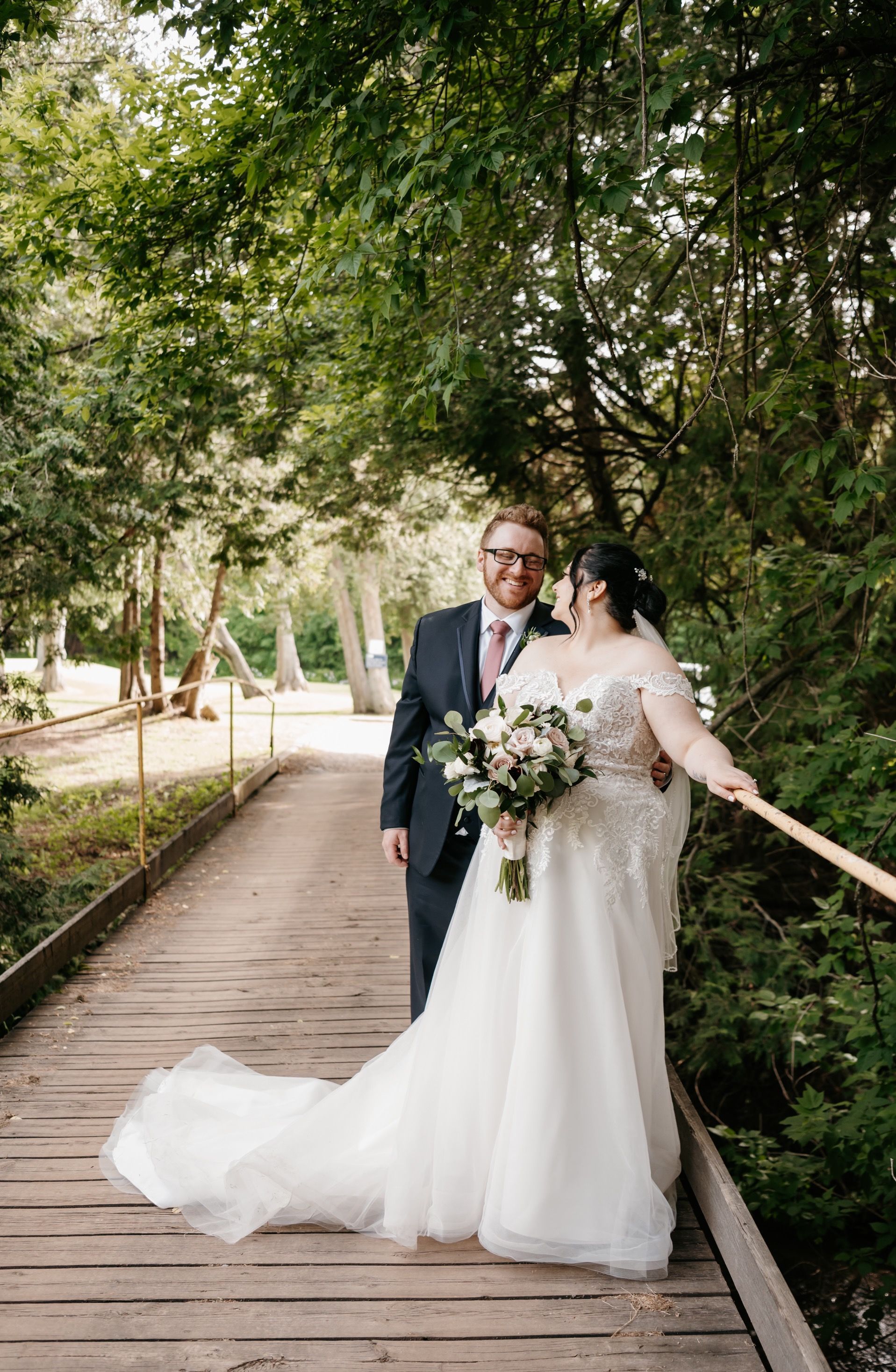 A bride and groom are standing on a wooden bridge.