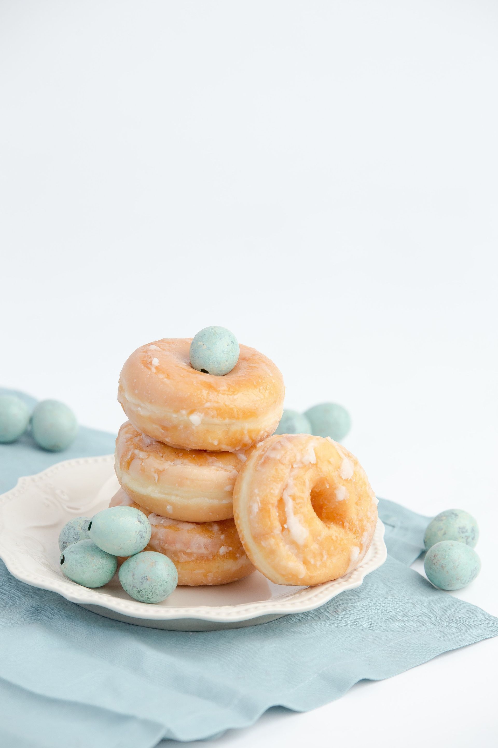 Three glazed donuts are stacked on top of each other on a plate.