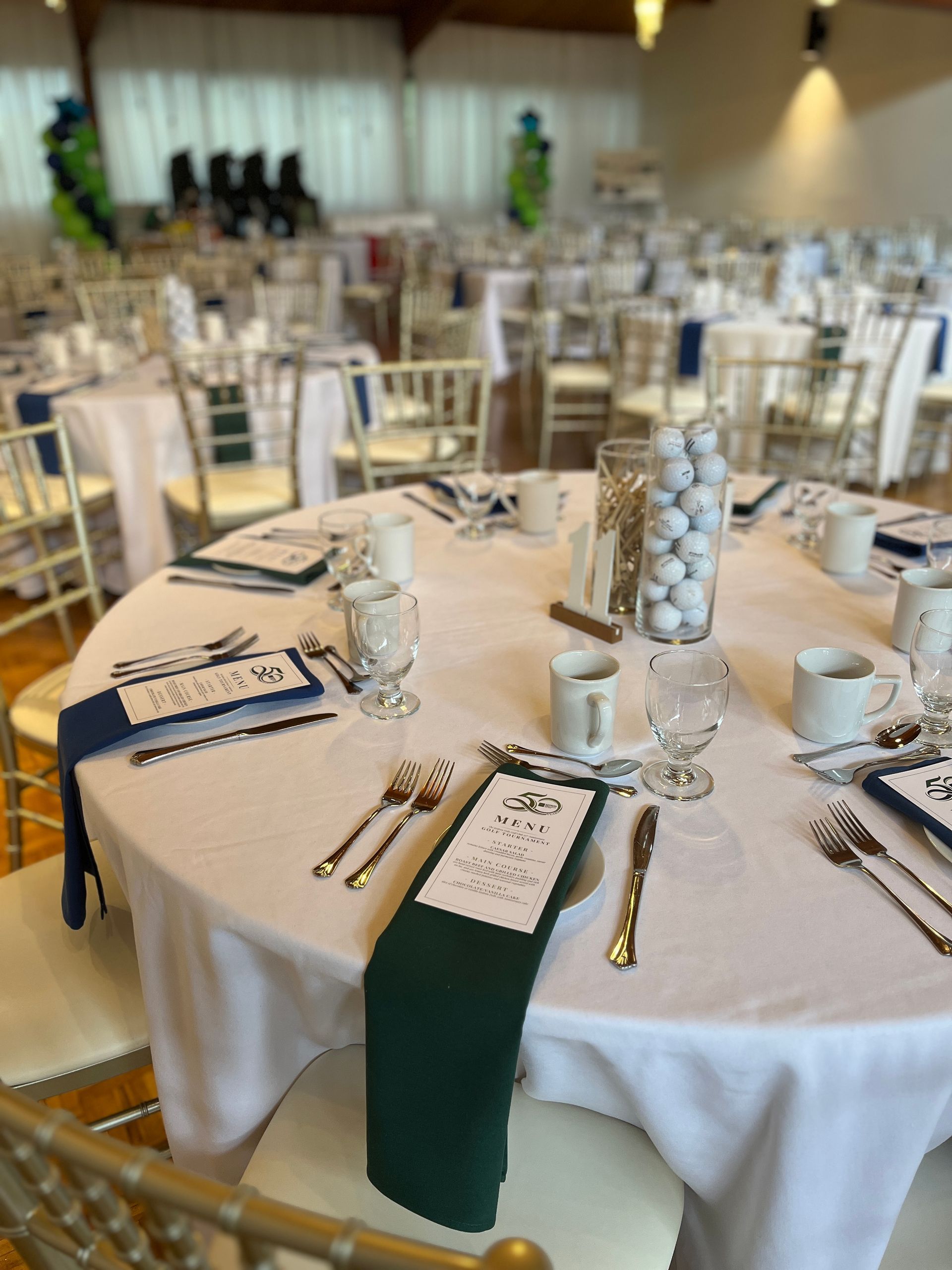 A table with a green and blue napkins and a vase of golf balls and a vase of tees as centerpieces.