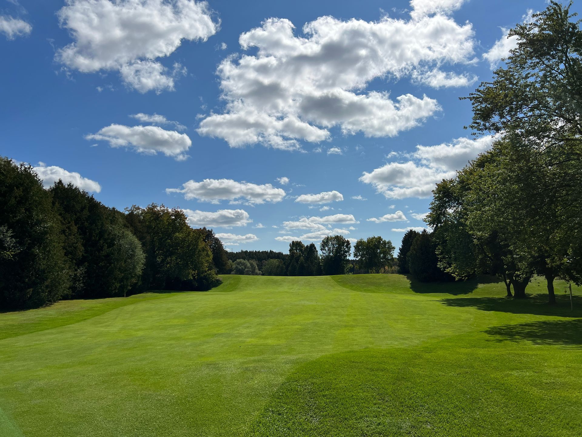 A golf course with trees and a blue sky with clouds.