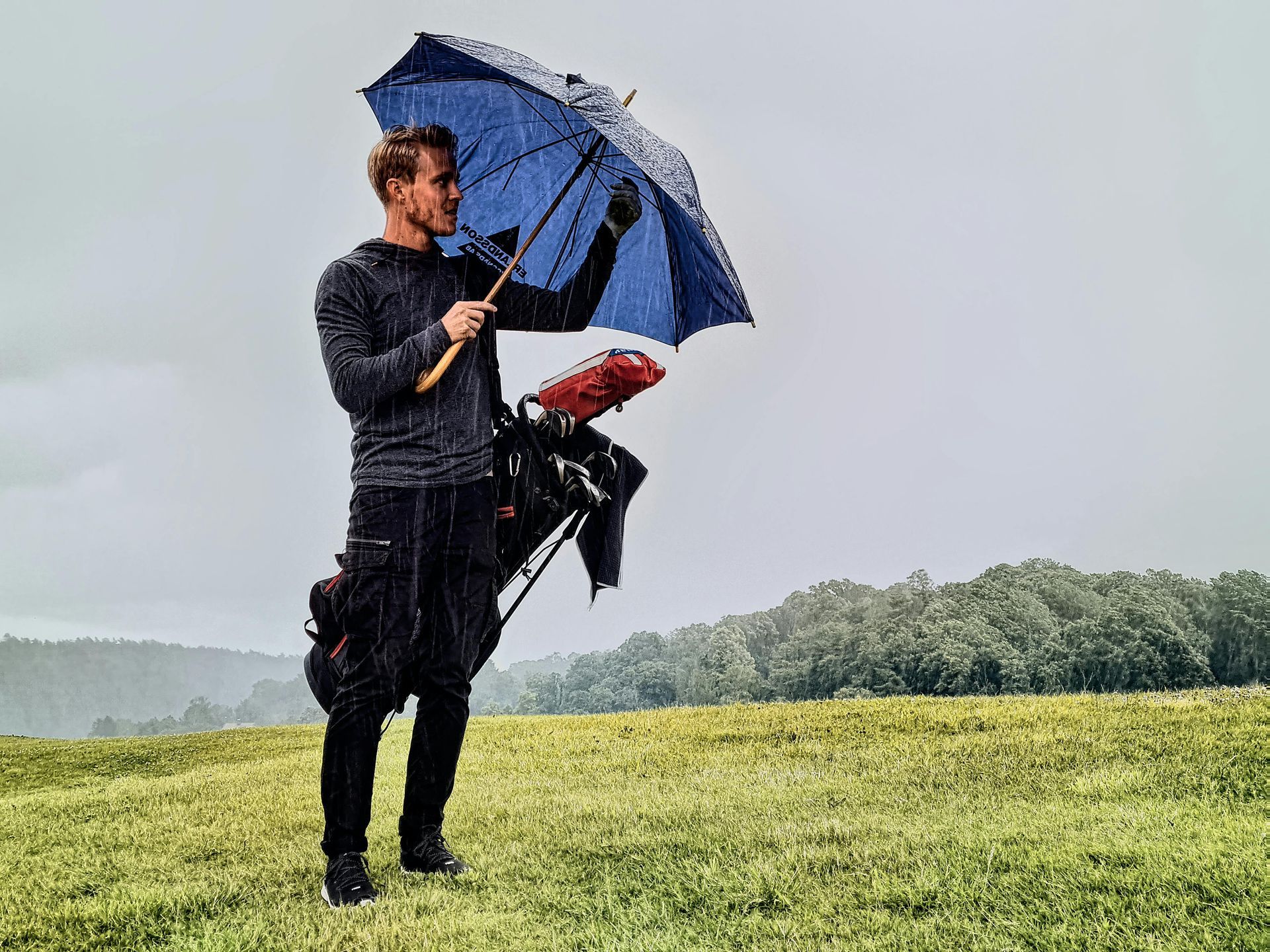 A man is holding an umbrella and a golf bag on a golf course.