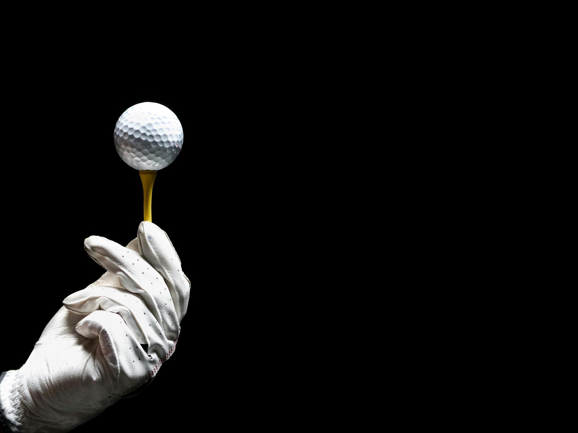 Gloved hand holding a golf ball on a tee, set against a black background.