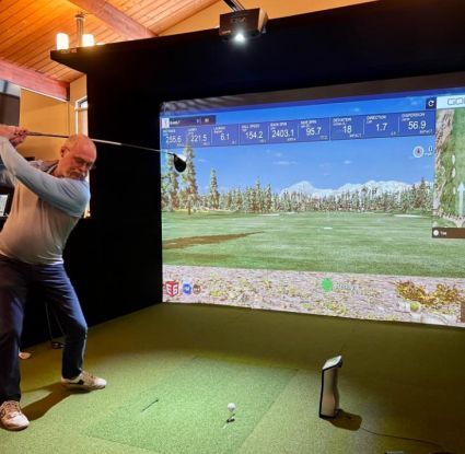 A man is swinging a golf club in front of a large screen/golf simulator.