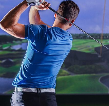 A man in a blue shirt is swinging a golf club in front of a simulator.