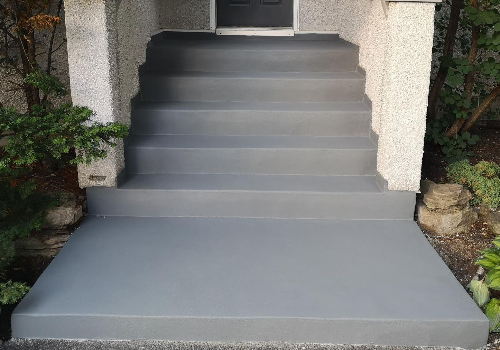 Gray painted concrete steps leading up to a door, flanked by textured columns.