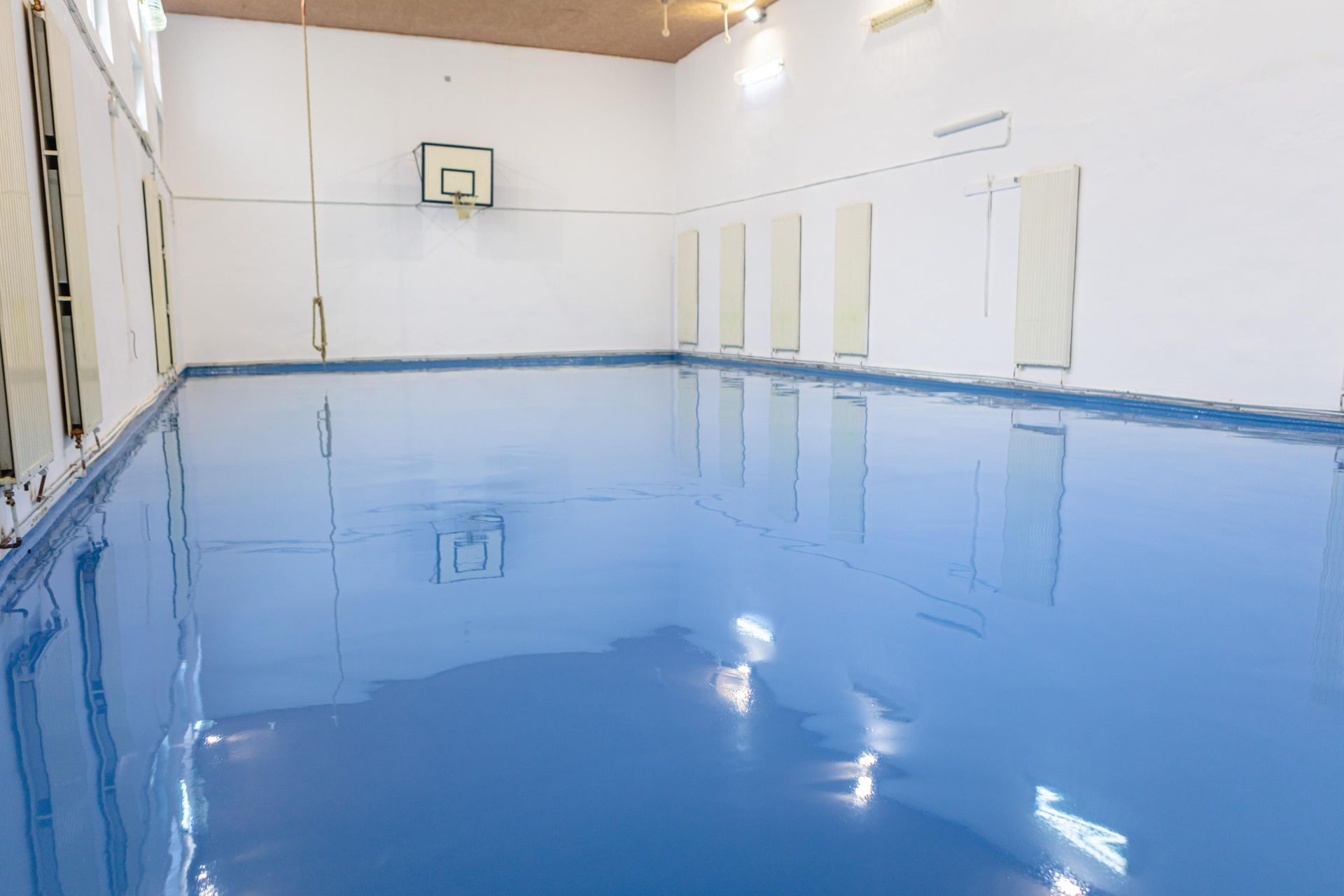 Blue epoxy floor in a gymnasium with a basketball hoop and white walls.
