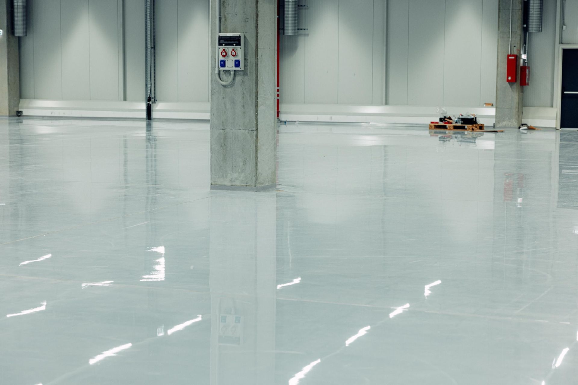 Large, empty, glossy white industrial floor with concrete support columns and equipment.
