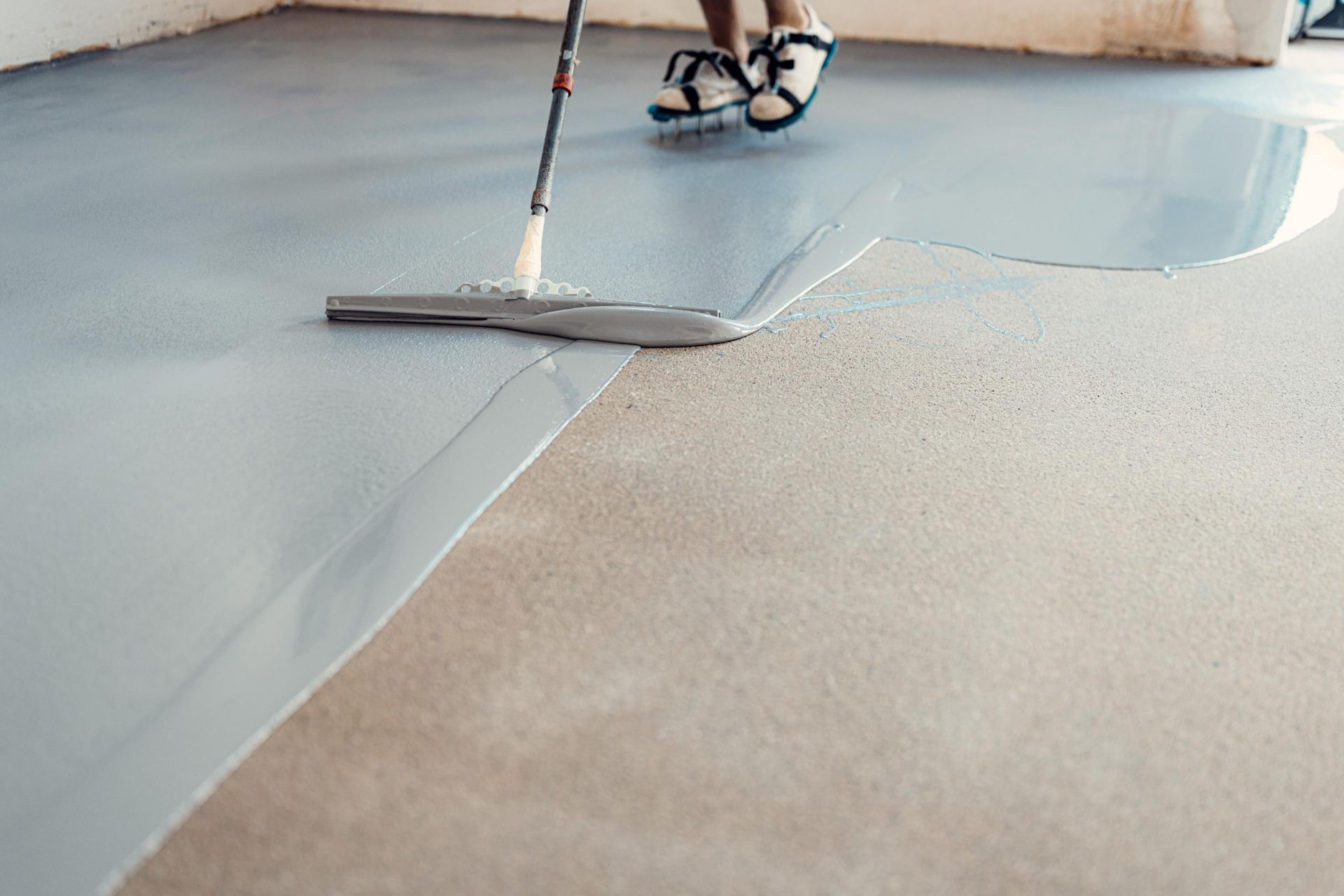 Person applying gray epoxy coating to a concrete floor with a squeegee.