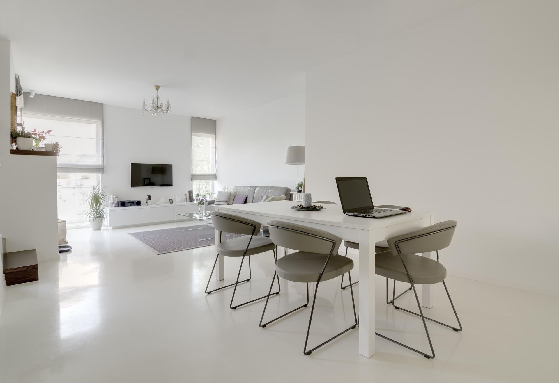 Modern, white-walled open-plan living and dining space; table with laptop, chairs, sofa, TV, and blinds.
