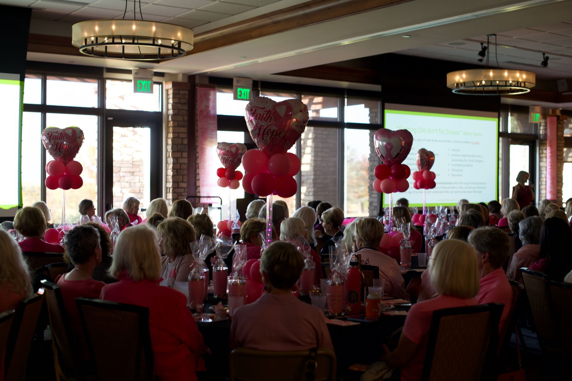 A large group of people are sitting at tables in a room with balloons in the shape of hearts.
