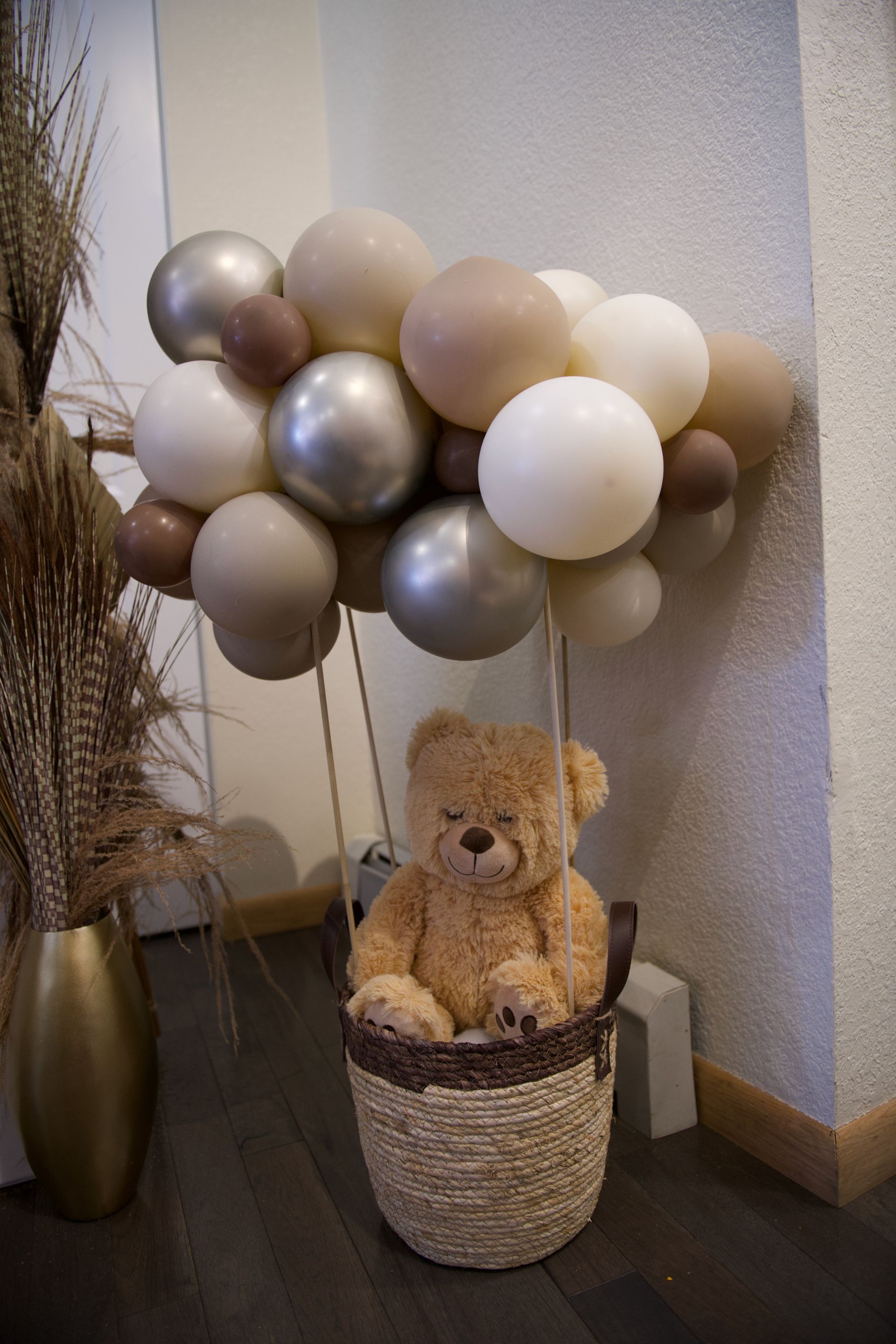 A teddy bear is sitting in a basket surrounded by balloons.