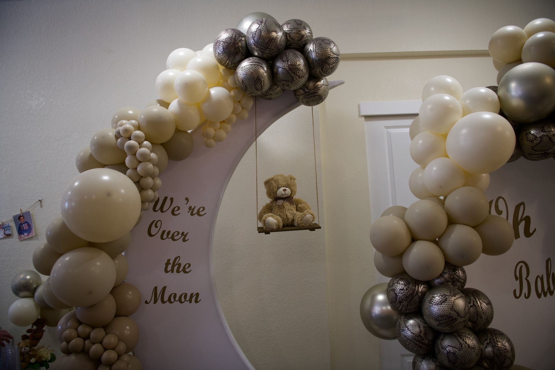 A teddy bear is sitting on a swing surrounded by balloons.