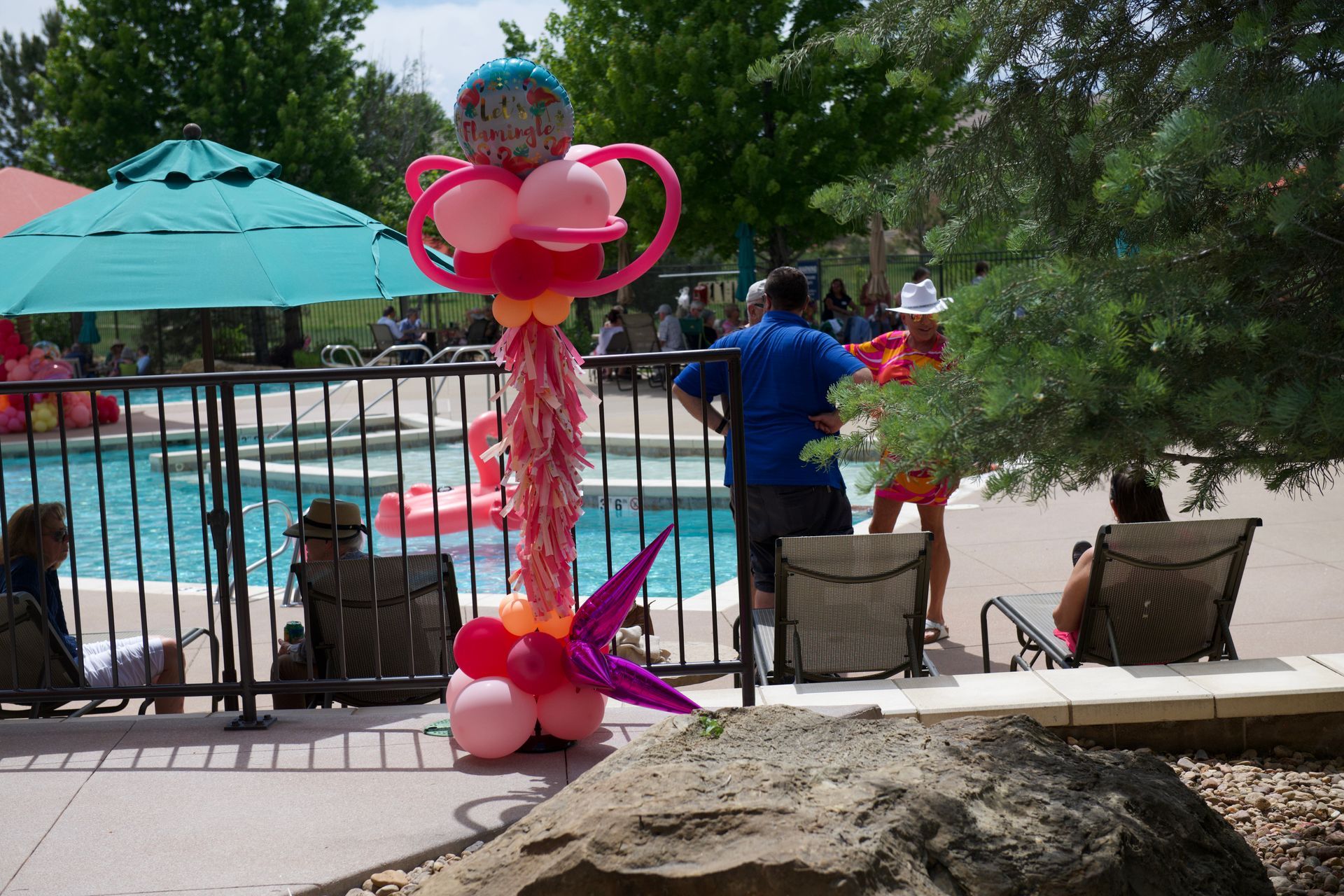 A group of people are sitting by a pool with balloons on a pole.