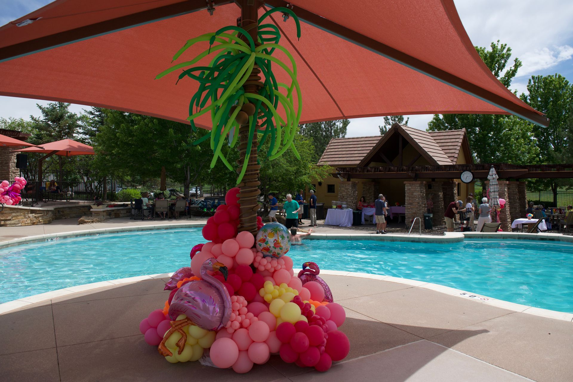 A palm tree made out of balloons is in front of a swimming pool.