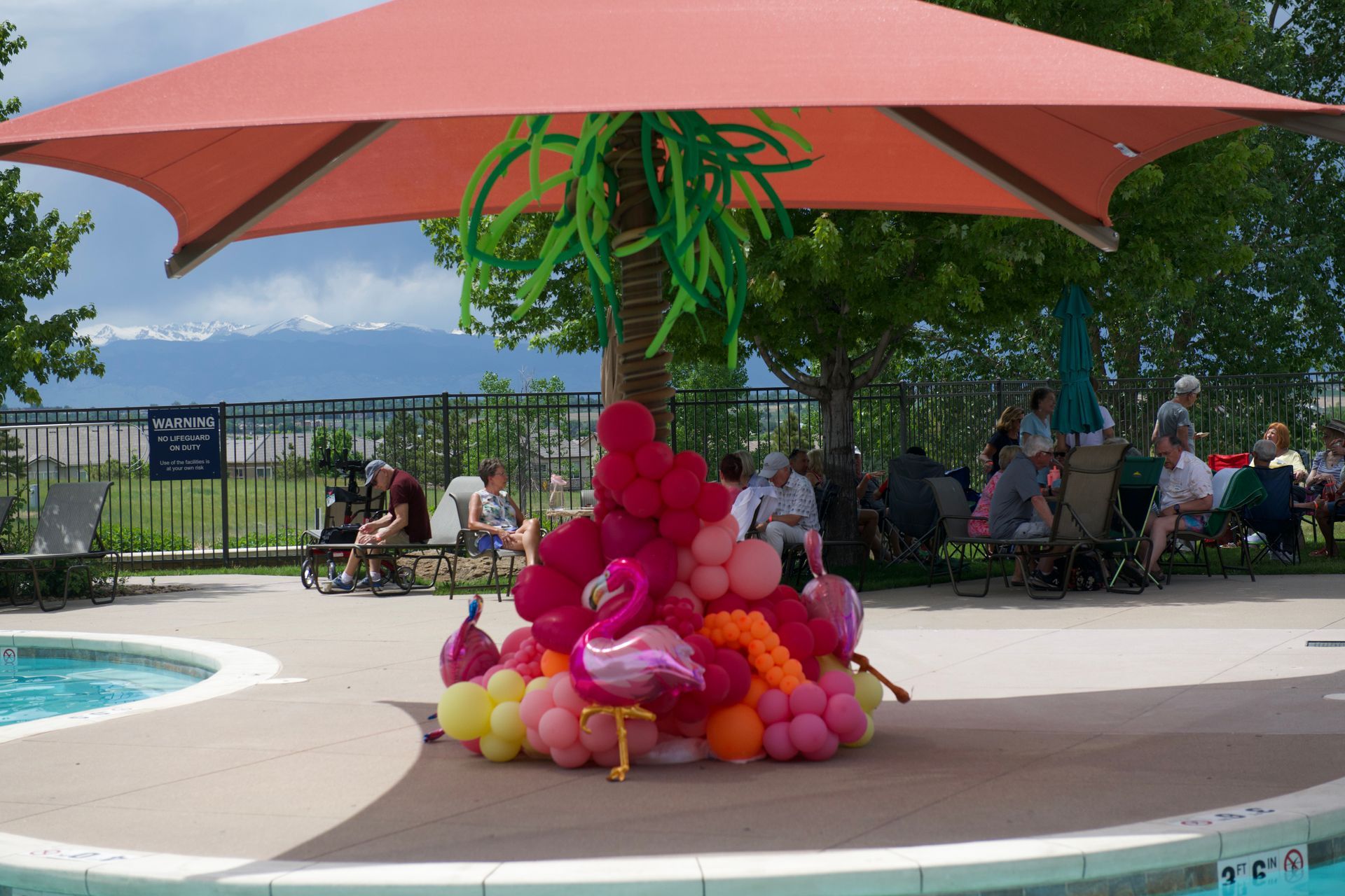 A bunch of balloons are sitting under an umbrella near a pool