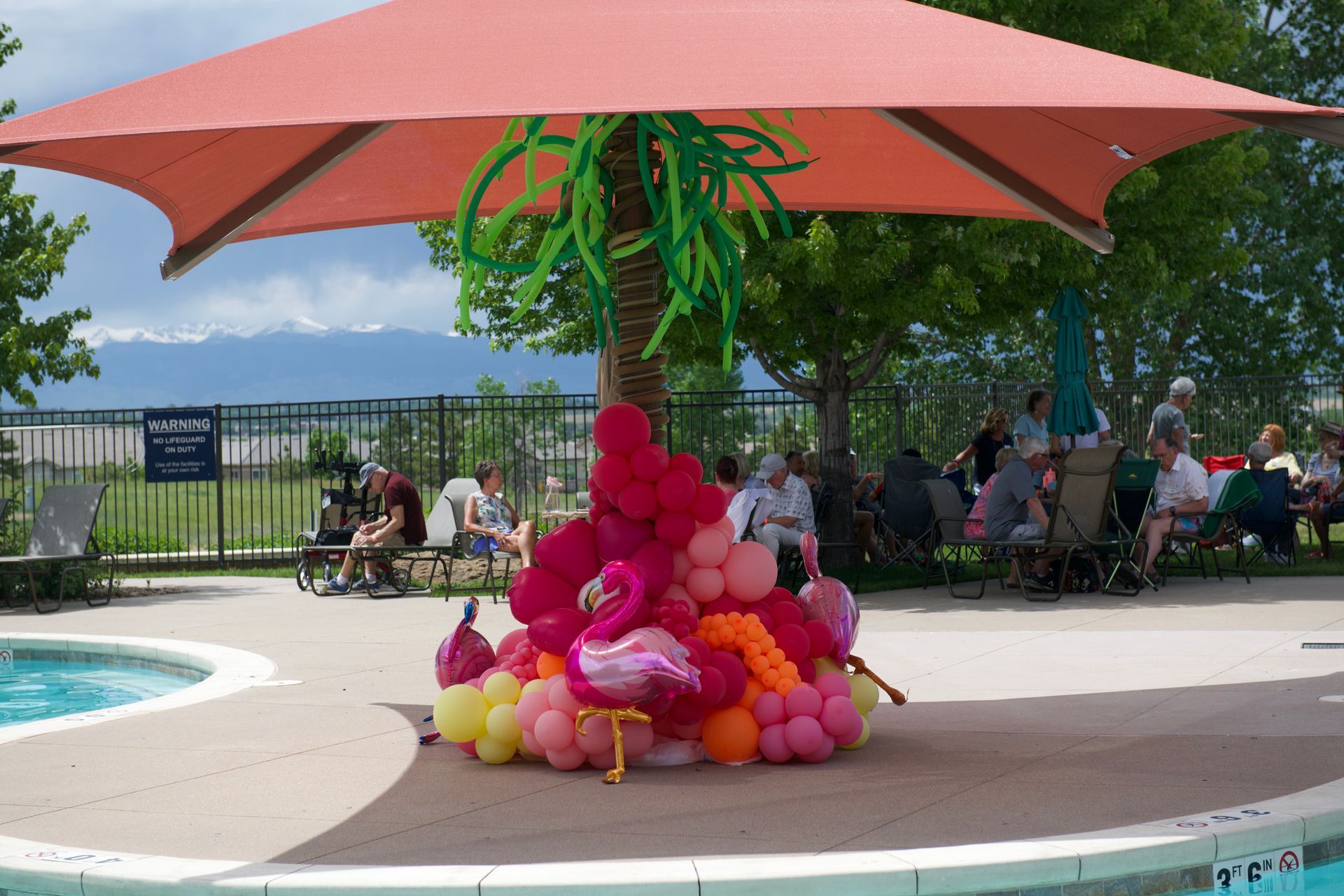 A bunch of balloons are sitting under an umbrella near a pool