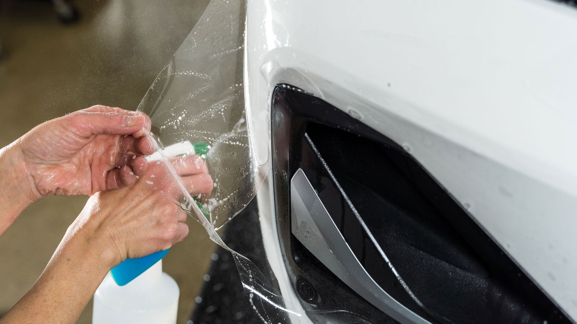 A person is applying a protective film to the front bumper of a car.