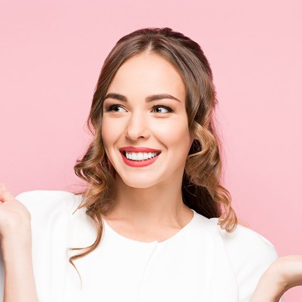 A woman in a white shirt is smiling on a pink background.