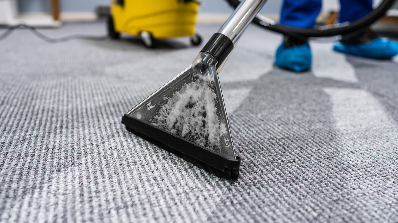Carpet cleaning nozzle scrubbing gray carpet, with a yellow cleaner in the background.