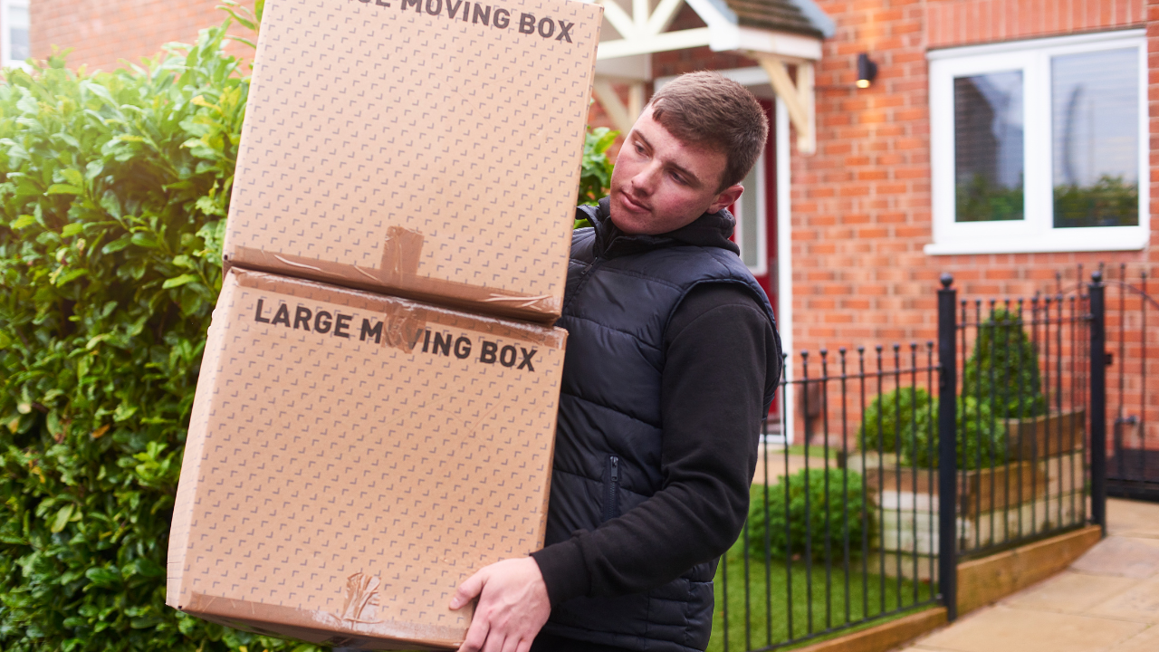 Man carrying a large cardboard moving box outside a brick house