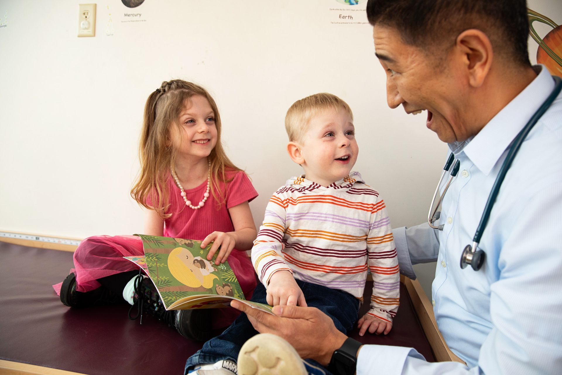 Doctor reading to two children in a medical office; all smiling.