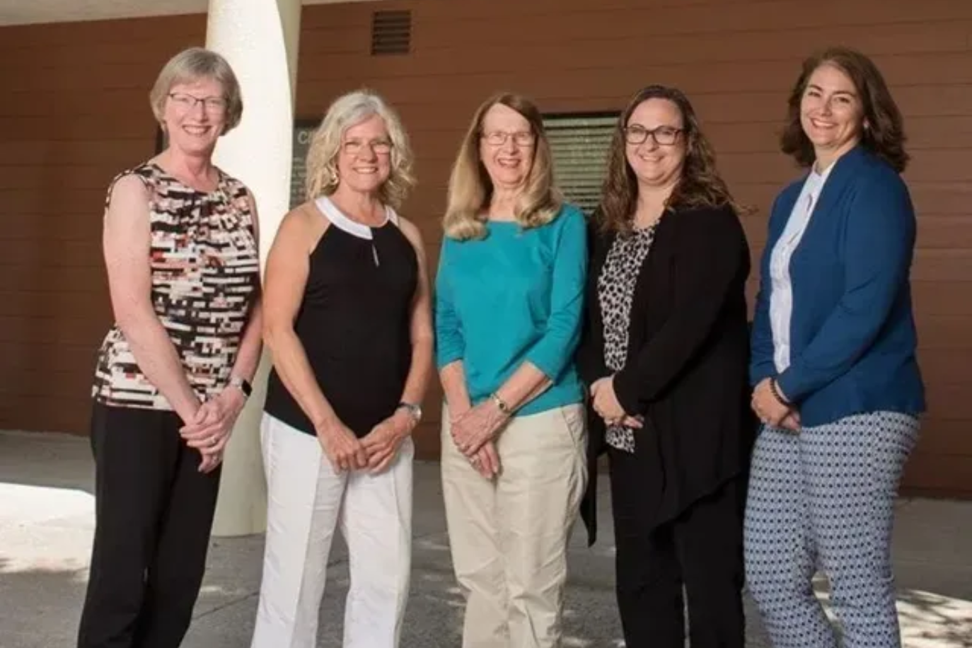 Five women standing together outdoors, smiling at the camera.