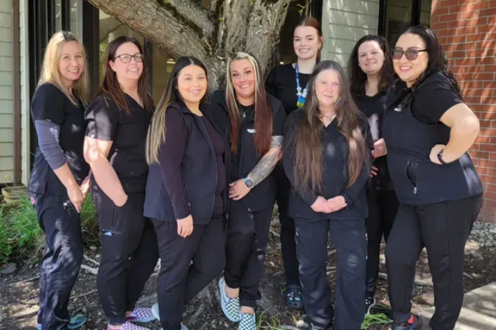 Group of people in black scrubs standing in front of a tree. They are smiling.
