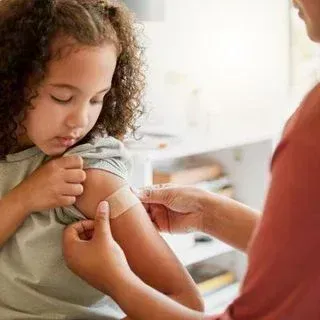 A person applying a bandage to a child's arm in a room with a blurred background.