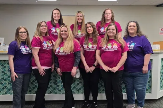 Nine people in matching shirts stand behind a counter.