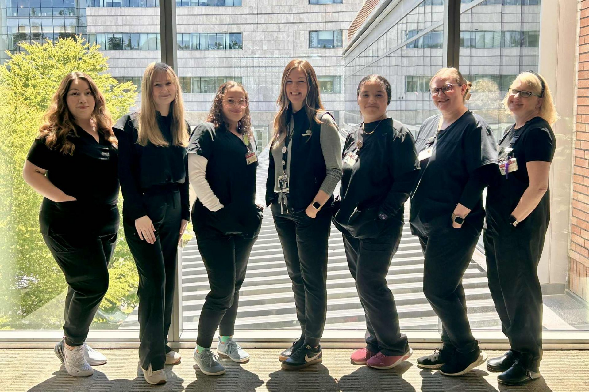Seven people in black scrubs stand by a window.