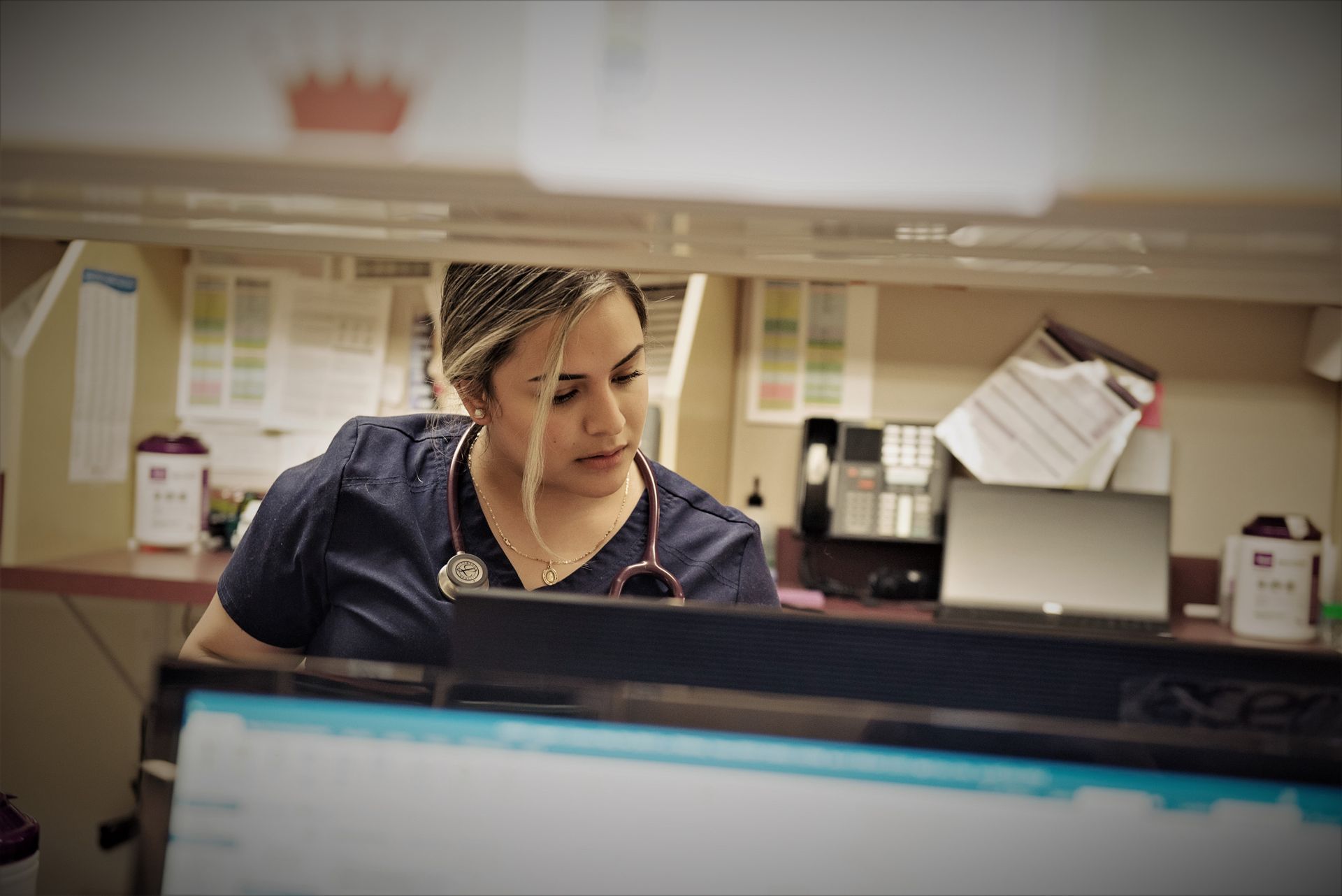 Healthcare worker leaning over a counter, looking at a computer screen in a medical office.