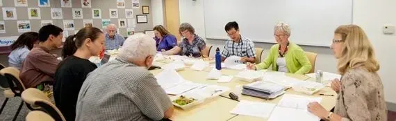 Group of people seated around a table, reading papers in a well-lit room.