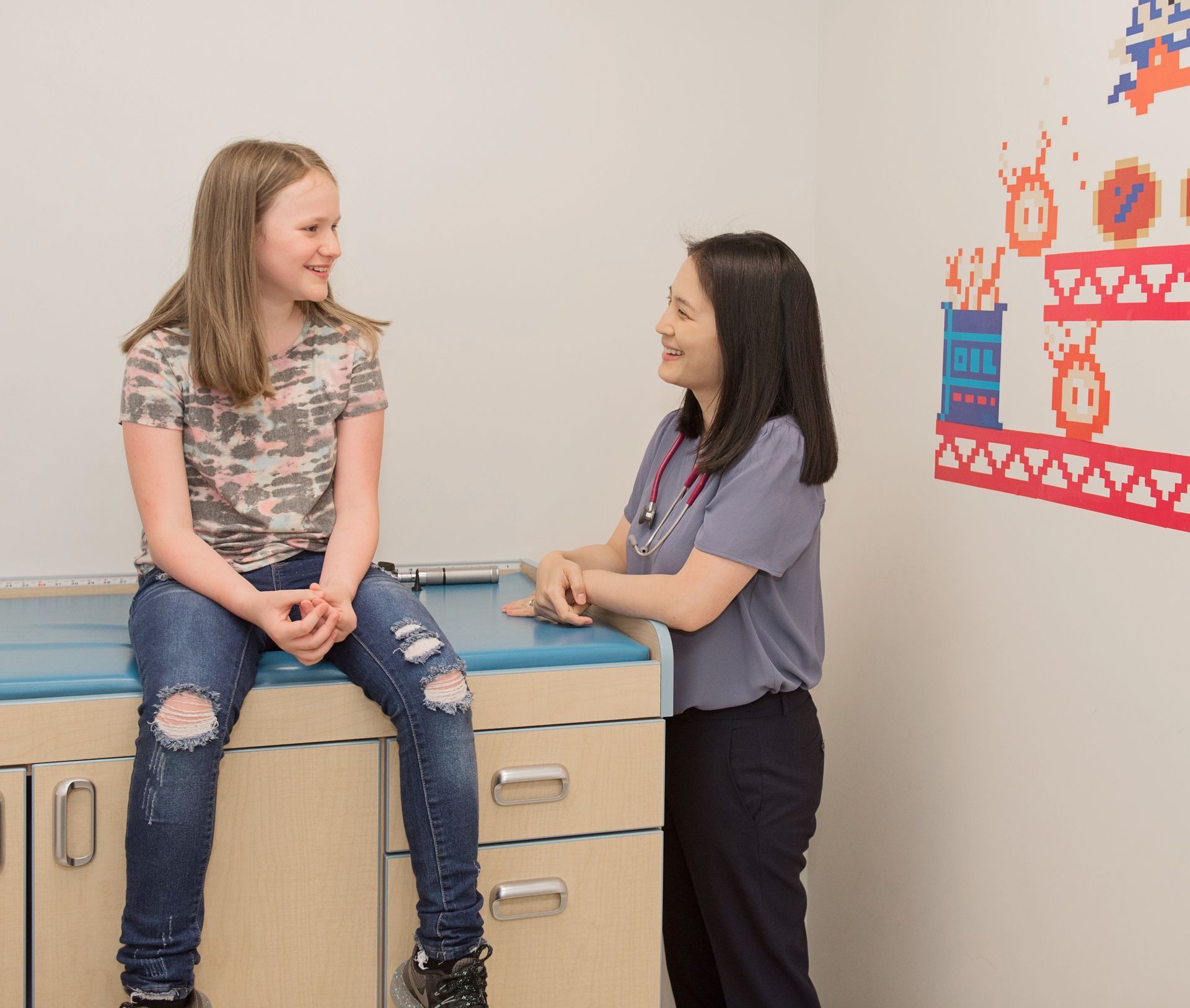 Girl sitting on exam table, talking to a doctor in a medical office.