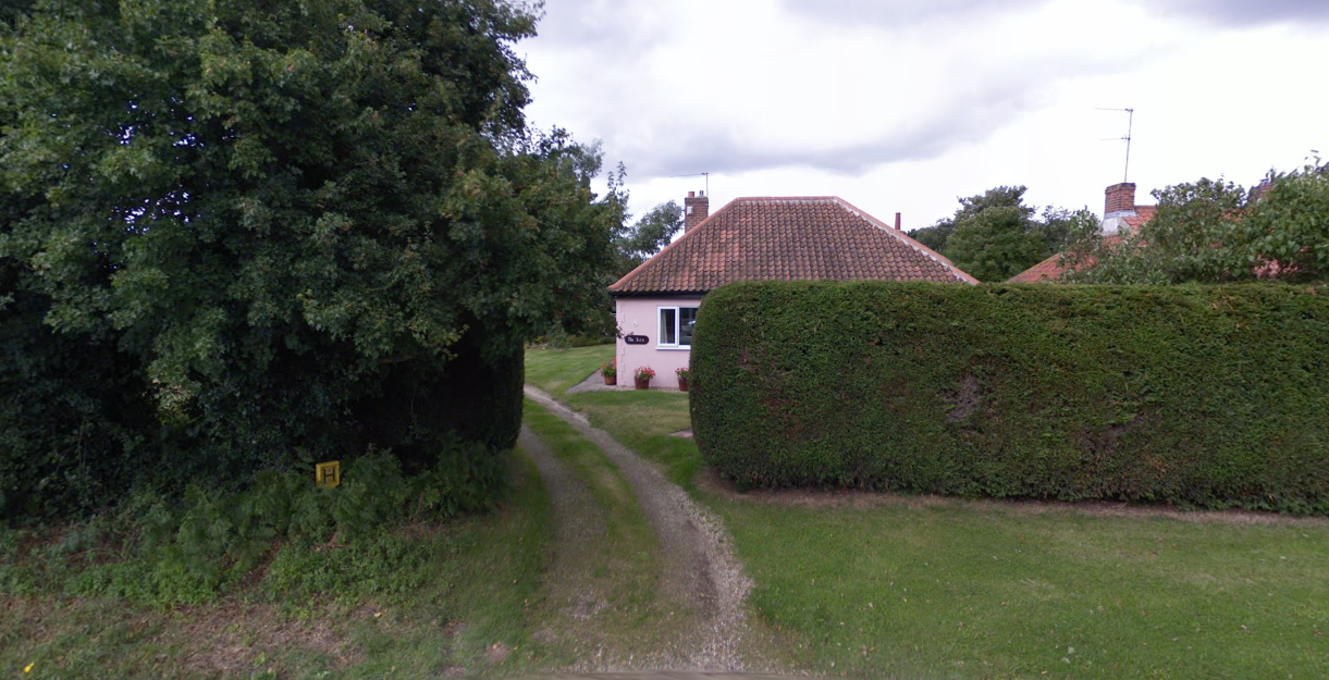 A dirt road leading to a house surrounded by trees and bushes.
