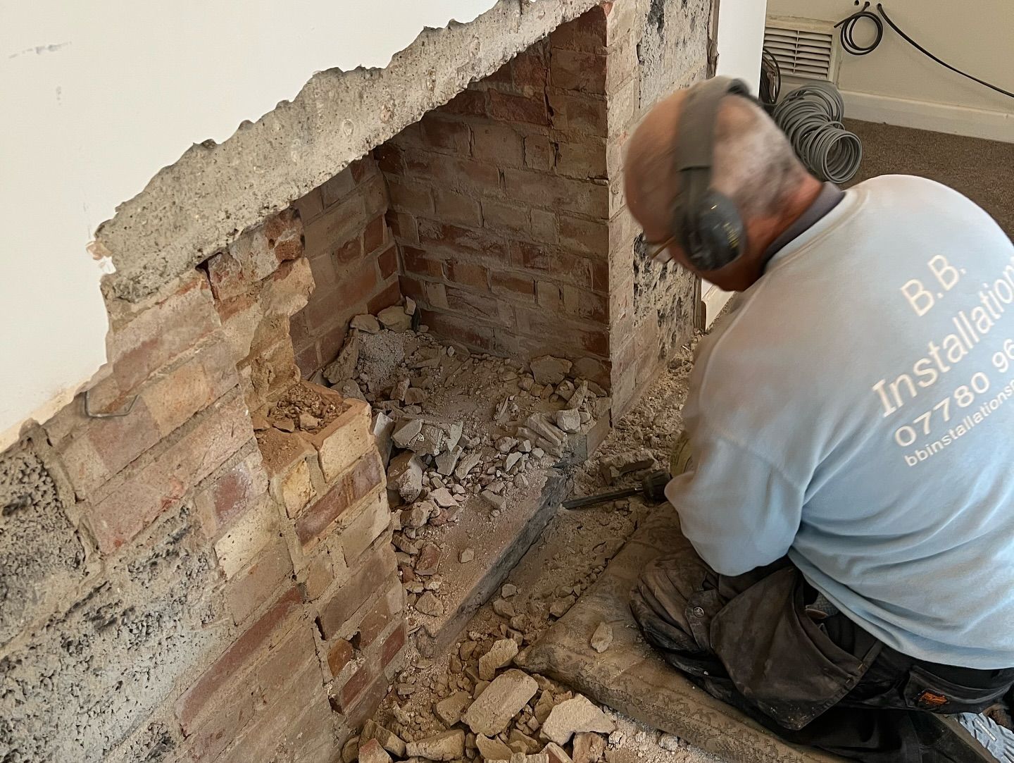 A man wearing headphones is working on a brick fireplace.