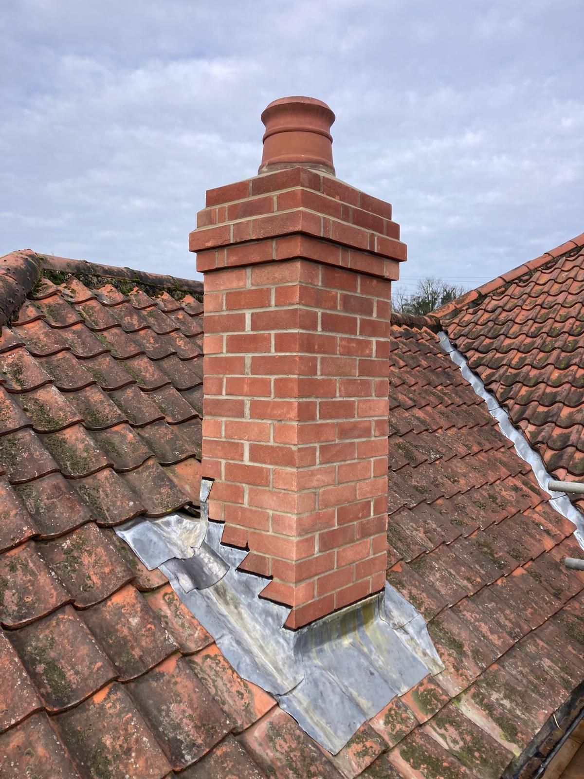A brick chimney is sitting on top of a tiled roof.
