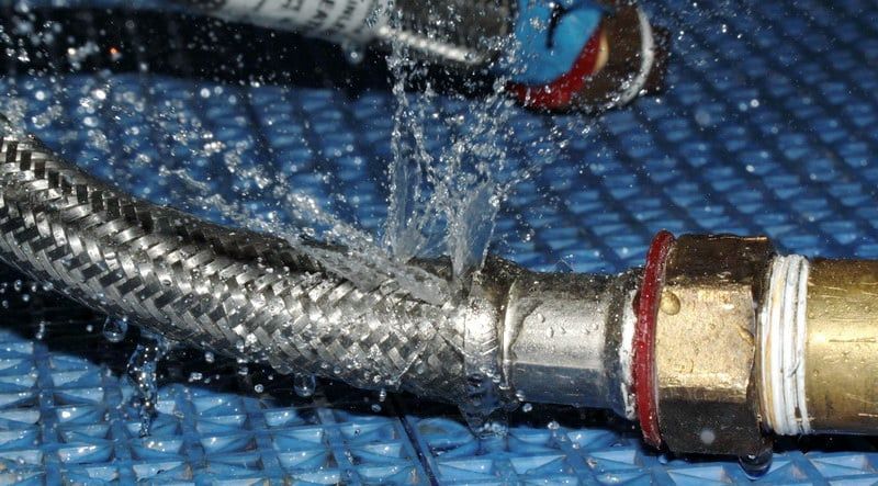 Water spraying from a damaged, braided metal hose connected to a brass fitting; close-up shot — Taps 'R' Us in Caboolture, QLD