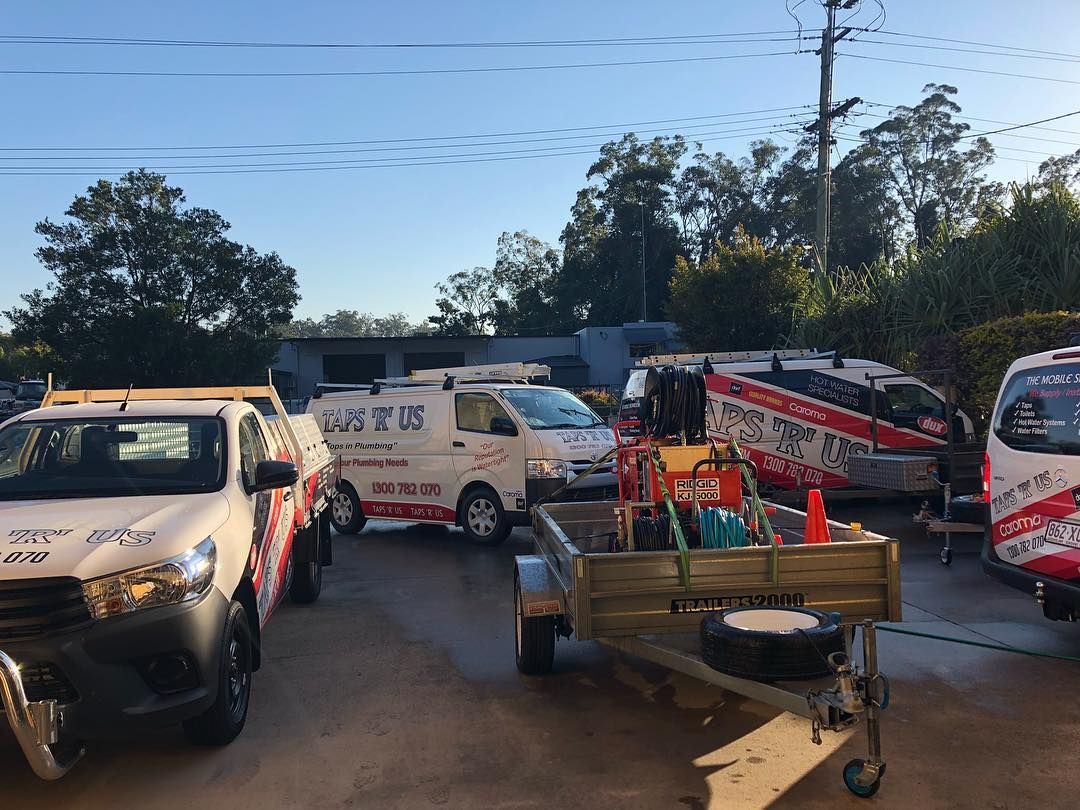 Vehicles parked outside a building. White vans and trucks with company logos, a trailer and clear blue sky — Taps 'R' Us in Noosa, QLD
